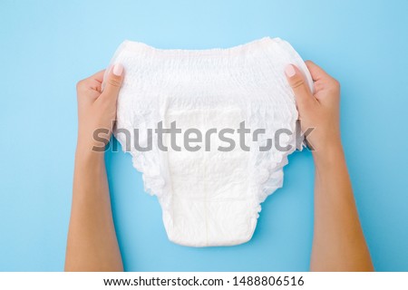 Woman hands holding white adult diaper on pastel blue background. Closeup. Point of view shot.