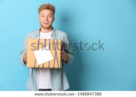 Happy young man with gift box on color background