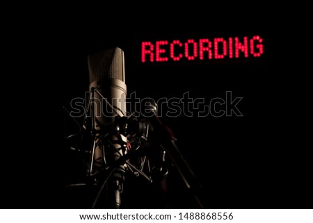 Microphone in dark studio in front of red recording backlit lettering