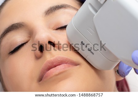 Woman receiving high intensity focused ultrasound treatment on face. Therapist doing cosmetic plasma lift on cheek with ultrasonic device. Royalty-Free Stock Photo #1488868757