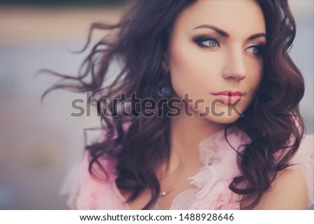 Close-up portrait of young slim beautiful smiling brunette woman in pink dress posing on sunset ocean beach. 
