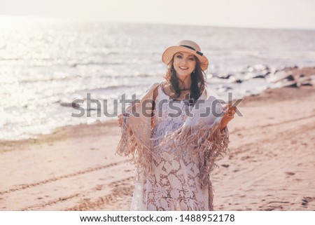 Portrait of happy smiling pregnant woman in white dress walking and relaxing on the beach at summer
