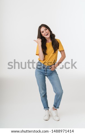 Full length image of young brunette woman wearing casual clothes smiling and pointing finger at copyspace isolated over white background
