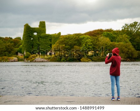 Girl teenager taking picture on her smart phone of Menlo castle, Ireland, Galway, Concept: tourist, adventure, technology,