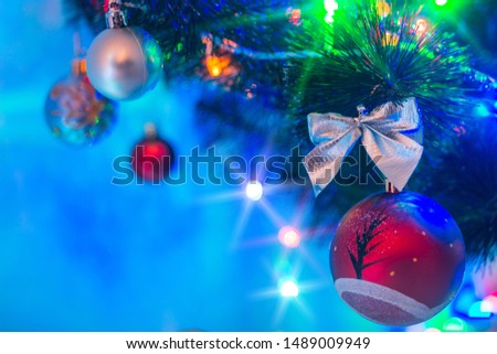 Christmas composition, spruce branch with beautiful toys, colorful bows and glowing lights of garland. Multi-colored glare and rays of luminous bulbs, lens flare, light effect on a blurred background