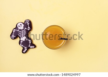 Delicious Ginger Biscuits for Halloween and Pimpkin Juice on Yellow Background Halloween Background One Gingerbread in Shape of Skeleton Horizontal View from Above