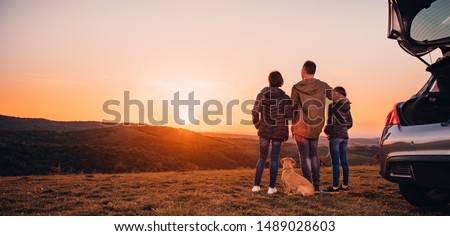 Family with small yellow dog embracing at hill and looking at sunset Royalty-Free Stock Photo #1489028603
