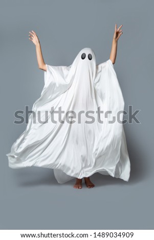 A girl in a Ghost costume on a gray background in the Studio. Halloween minimal concept.