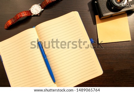 Flat lay of blank page of opened notebook, blue pen, mechanical watches with brown band, old film camera and photo envelop. Photo content plan, travelling planning concept or business plan. 