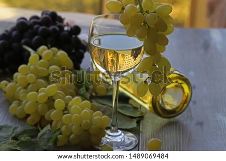 White wine, glass, white grapes and black grapes on wooden table.