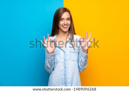 Young woman over colorful background showing an ok sign with fingers