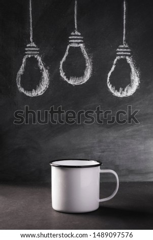 A group of light bulbs sketched in white chalk behind an empty tin mug signifying potential.