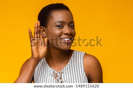 Curious interested african american woman holding hand near ear and trying to hear information, yellow studio background Royalty-Free Stock Photo #1489155620