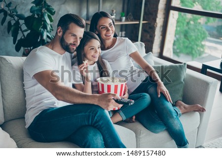 Portrait of nice attractive lovely charming cheerful cheery family wearing casual white t-shirts jeans denim sitting on divan having fun watching series serial video switching channel indoors