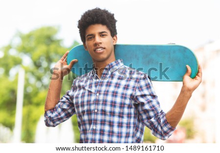 Portrait of handsome african american teen guy posing with modern skateboard outdoors