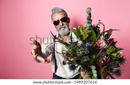 Stylish bearded man in sunglasses of middle age holds a bouquet of flowers. smiles at the camera and points at you. come with me