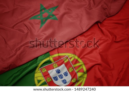 waving colorful flag of portugal and national flag of morocco. macro