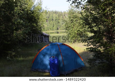 Log cabin on the shore of the pond and a wooden fishing boat.Mirror image of the forest in the lake.Bathhouse near water.Tourist tent.Summer holidays in the wildlife of Karelia.Quiet relaxation.