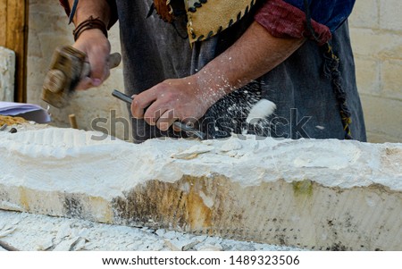 Stonemason With Ancient Costume During The Processing Of The Stone With Chisel. In evidence a fragment of stone that squirts Royalty-Free Stock Photo #1489323506