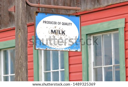 Weathered and marked, a retro sign hangs in front of a red barn touting quality milk. 