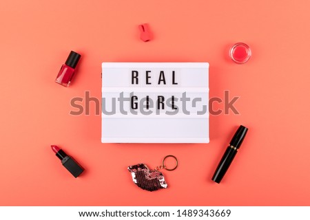 Real girl text on lightbox and decorative cosmetics on coral background. Beauty, makeup flat lay
