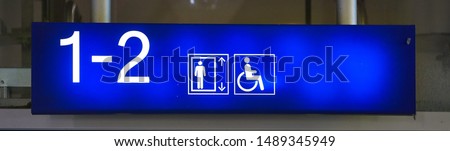 Neon sign with wheelchair symbol in the direction of the elevator at a train station.