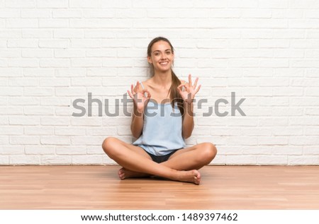 Young woman sitting on the floor showing an ok sign with fingers