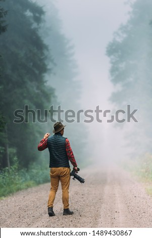 Man photographer holding camera in the forest during morning dog .
