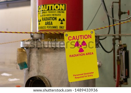Ionizing radiation hazard symbol, caution radiation area and personnel dosimeter required text on yellow warning sign displayed on the equipment that produces dangerous ionizing radiation  Royalty-Free Stock Photo #1489433936