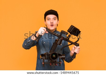 An operator with an open mouth is surprised when something shot on a dslr camera on an orange background. A young videographer using stabilization for a camera. Close-up portrait