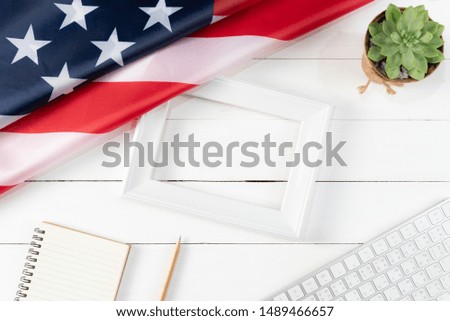 Top view of keyboard, book, pencil, white photo frame and American flag on white wooden background. Happy Labor Day.