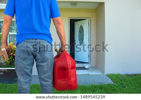 Arsonist man with red plastic gasoline can container and box of striking matches preparing to commit arson crime and maliciously and  intentionally burn down a house with an open front door. Royalty-Free Stock Photo #1489545239