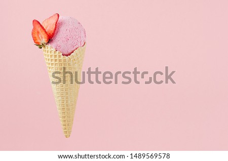 Pink creamy ice cream in crisp waffle cone with strawberry slices on pastel pink background, copy space.