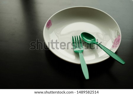 Plates, tiles with green plastic cutlery, black backdrop