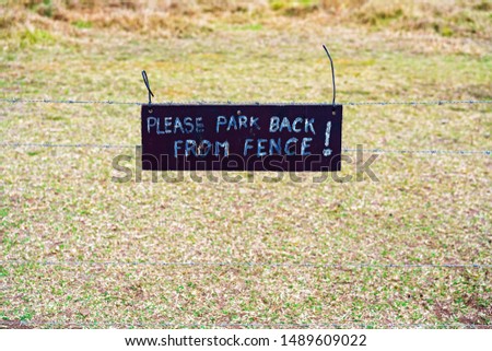 Please Park Back From Fence handwritten sign on barbed wire fence on a farmer's rural property
