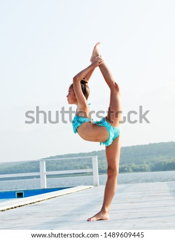 Gymnast little girl child doing acrobatic exercises outdoors on a beach in summer day