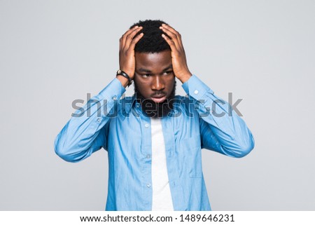 Studio shot of black man posing on background of white wall, dressed casually, expressing shock and despair, touching his head with both hands, screaming with mouth wide opened and eyes popped