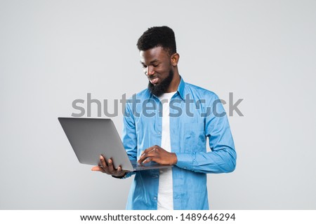 Young smiling african man standing and using laptop computer isolated over gray background