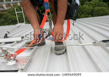 Clipping industrial lock Karabiner connected with fall arrest shock absorbing safety lanyard device into horizontal lifeline steel cable system permanent runs through multiple fixed roof anchor point