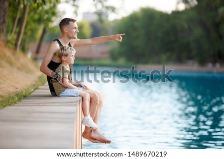 Photo of father and boy sitting on wooden bank by river