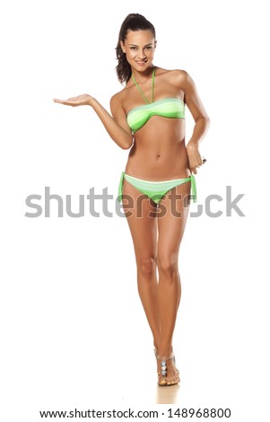 smiling pretty and beautiful young brunette in a bikini holding and advertises imaginary object