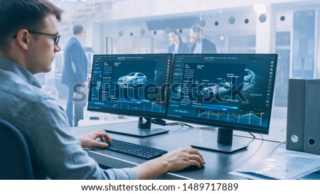 Professional Engineer Works on a Computer with a 3D CAD Software and Tests the Electric Car Chassis Prototype with Wheels, Batteries and Engine Standing in a High Tech Development Laboratory. Royalty-Free Stock Photo #1489717889