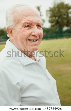 A portrait of a senior man smiling at a bowling green, looking away.