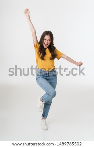 Full length image of excited brunette woman wearing casual clothes laughing and rejoicing with arms raised isolated over white background