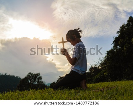 little girl praying to the GOD while holding a crucifix symbol with bright sunbeam on the sky