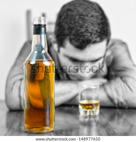 Whisky bottle with an out of focus drunk man in the background (only the bottle and the glass have color) Royalty-Free Stock Photo #148977650