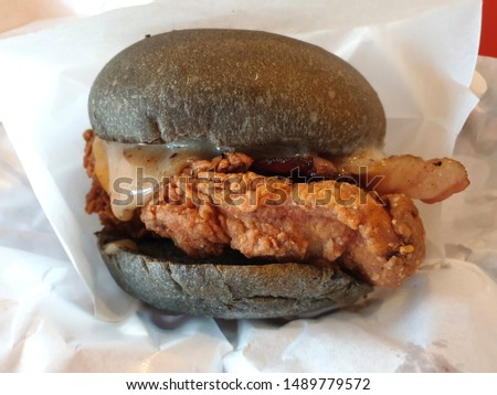 Top view  black charcoal burger with fried chicken meat topped with cheese and fresh vegetables.
