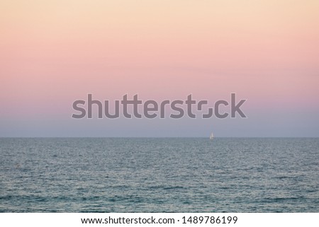 Waves breaking on a smooth shoreline of a sand beach in soft natural light with clouds in a sunset sky