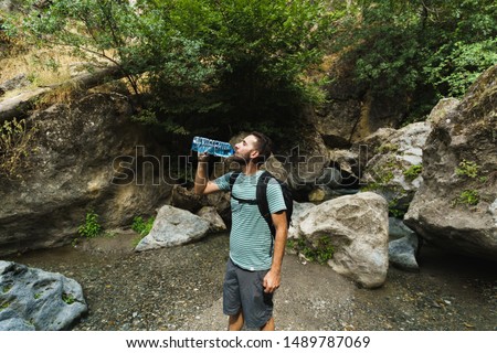 Man with beard drinking water from plastic bottle and enjoying mountain sunset. He is waring black backpack. Royalty-Free Stock Photo #1489787069