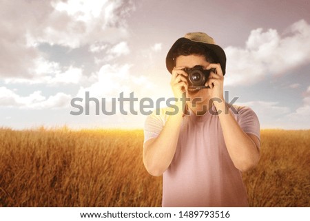 Asian man in hat take a picture with his camera on the grass field